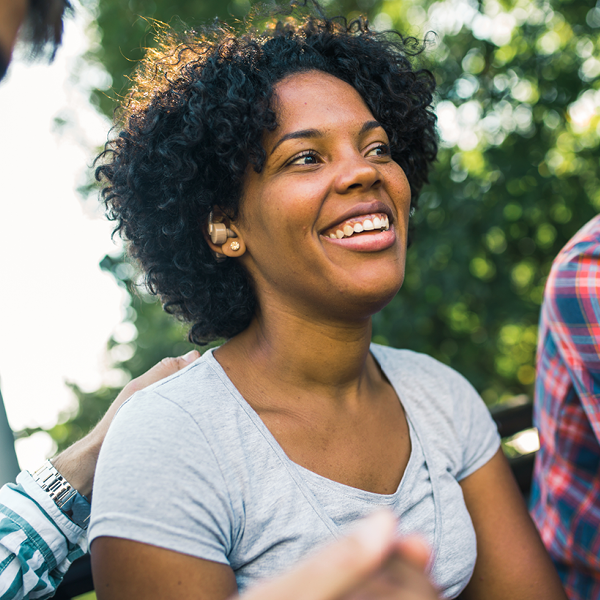 Smiling woman wearing a hearing aid device while enjoying time outdoors with friends.