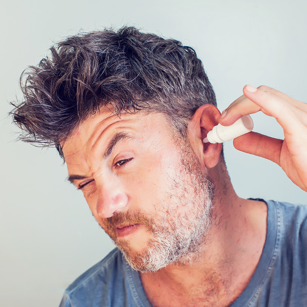 Man applying ear drops into his ear to address earwax buildup or ear discomfort.