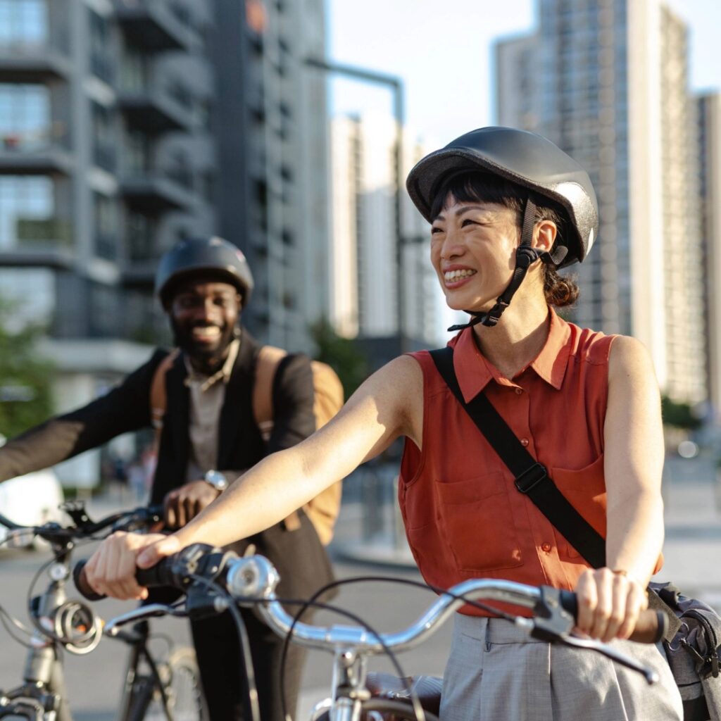 Two adults riding bicycles in a city environment, both wearing protective helmets highlighting the importance of headgear to help prevent traumatic injuries.
