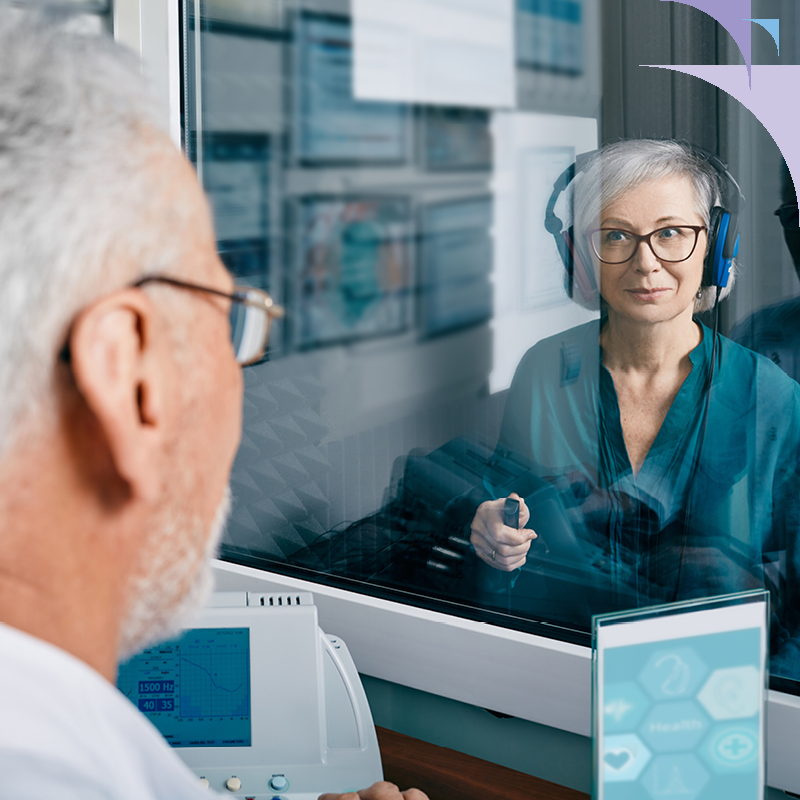 Senior woman undergoing a pure-tone audiometry test in a soundproof booth, wearing headphones for hearing evaluation.