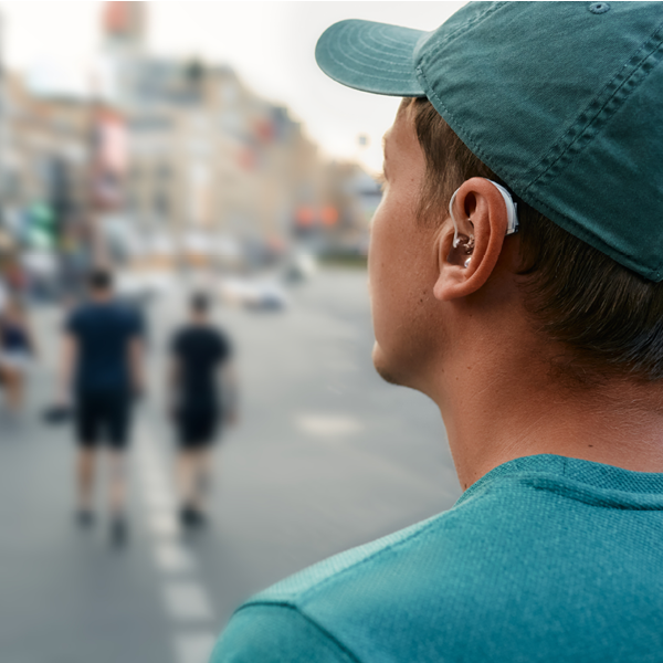 A person wearing a discreet behind-the-ear hearing aid while walking outdoors in a busy city environment.