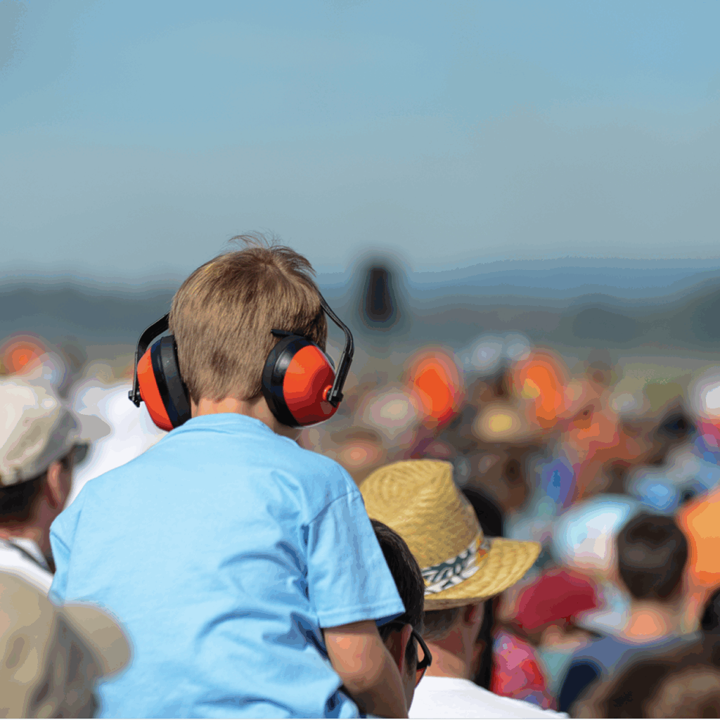 Young child wearing noise-reducing earmuffs on a parent’s shoulders at the Indy 500