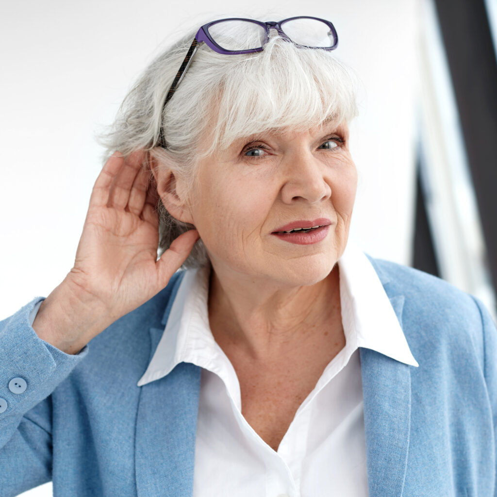 Older woman cupping her ear and leaning forward, a common sign of untreated hearing loss.