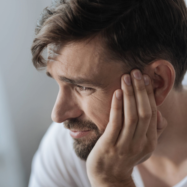 Man holding his ear with a pained or concerned expression, possibly experiencing symptoms of tinnitus or ear discomfort.