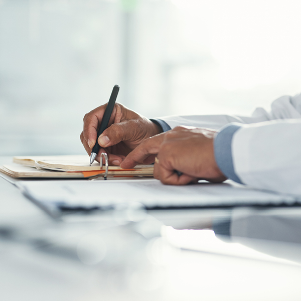 Close-up of a hearing care provider’s hands writing notes during a patient appointment.