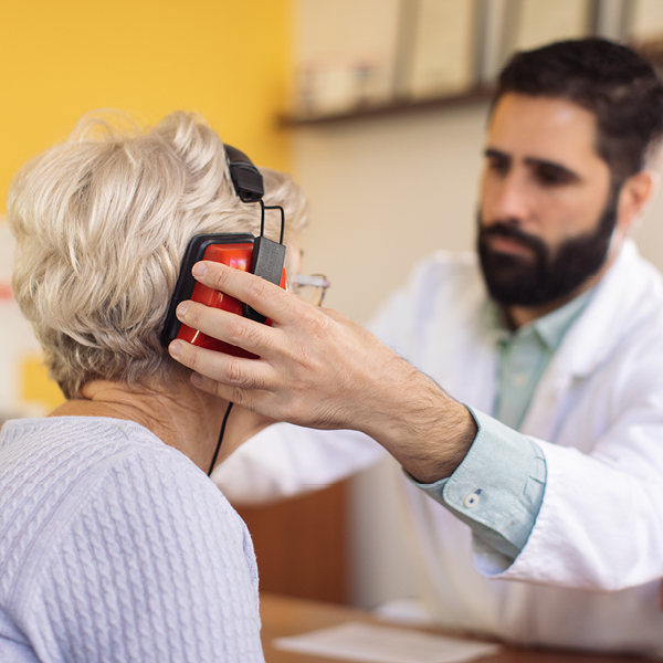 Hearing care professional performing a hearing test on an woman, placing red headphones on her ears in a clinical setting.