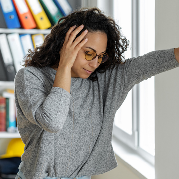 A woman steadies herself against a wall while holding her head, depicting dizziness and balance issues that can occur as side effects of ototoxic medications.