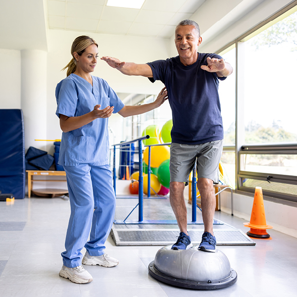 A clinician assists a patient with balance exercises, illustrating how ototoxicity can impact balance and the need for rehabilitation as part of monitoring and care.