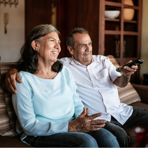 A couple relaxes on the couch, smiling while watching television together.