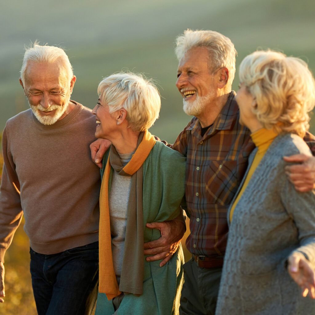 Group of older adults standing closely together outside, smiling and talking as they enjoy time together.