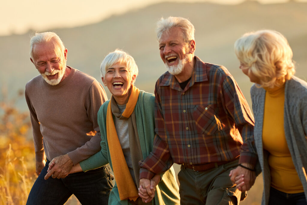 Four older adults walking hand in hand through a sunlit field, laughing and enjoying a shared moment.