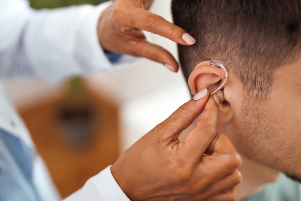 Hearing care professional placing a behind-the-ear hearing aid on a patient during an in-office fitting and adjustment.