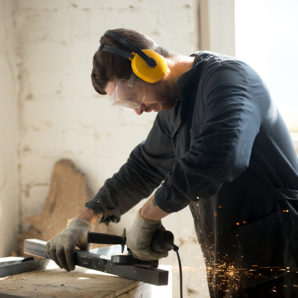 Worker using a power tool while wearing earmuffs and safety glasses to protect against loud noise.
