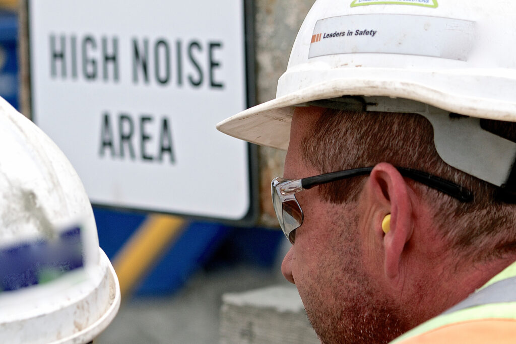 Construction worker wearing earplugs and a hard hat in a posted high-noise work area.