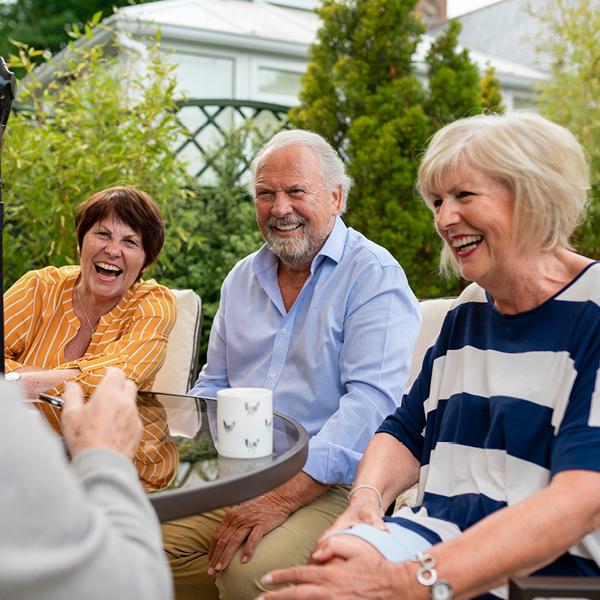 Group of adults laughing together at an outdoor table, highlighting meaningful conversation, friendship, and shared community experiences.