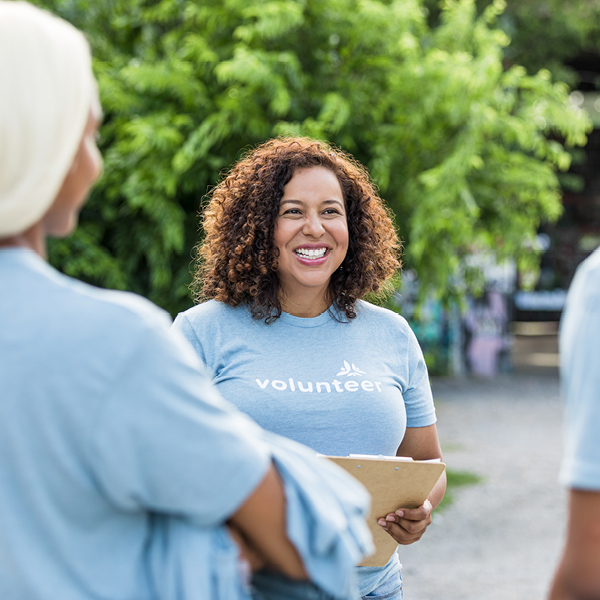 Community volunteer smiling and talking with others while holding a clipboard, representing open communication, inclusion, and community involvement.