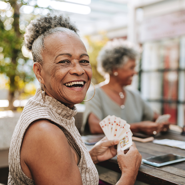 A woman smiling while playing cards with friends outdoors, showing joy, connection, and social engagement in a community setting.