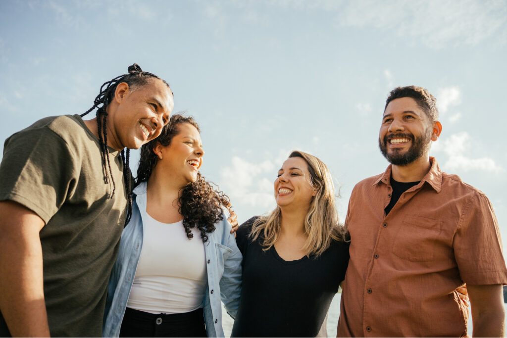Diverse group of adults standing close together outdoors, smiling and talking, symbolizing connection, belonging, and inclusive communication within a community.