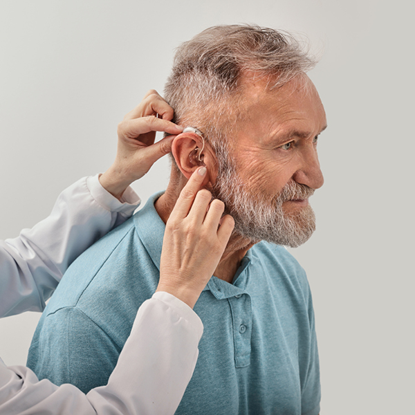 Hearing care professional fitting a hearing aid on an aging adult to support communication, brain health, and reduced risk of cognitive decline.
