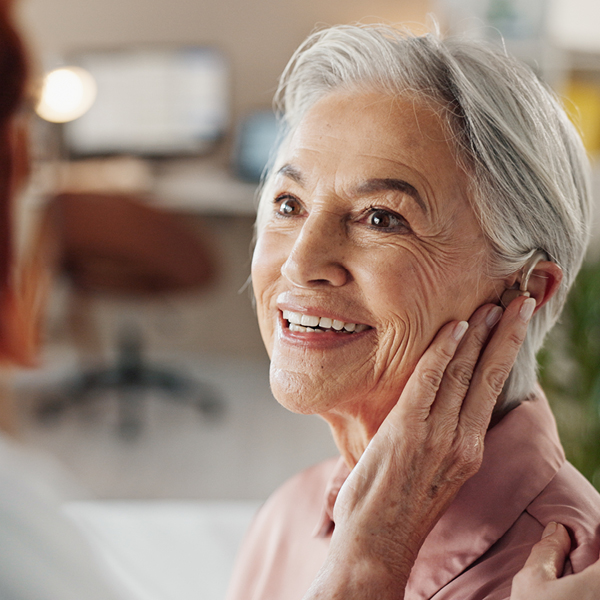 Older woman gently touching her ear, illustrating awareness of hearing changes and the experience of listening effort in daily life.