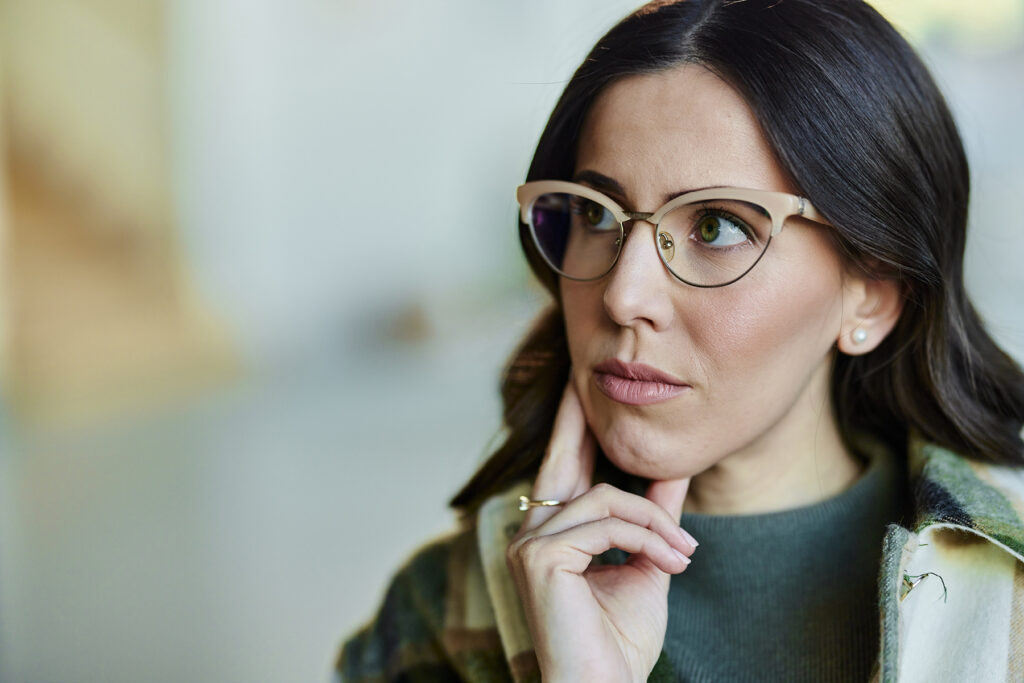 Middle-aged woman wearing glasses looking thoughtfully to the side, representing vision and hearing health awareness.
