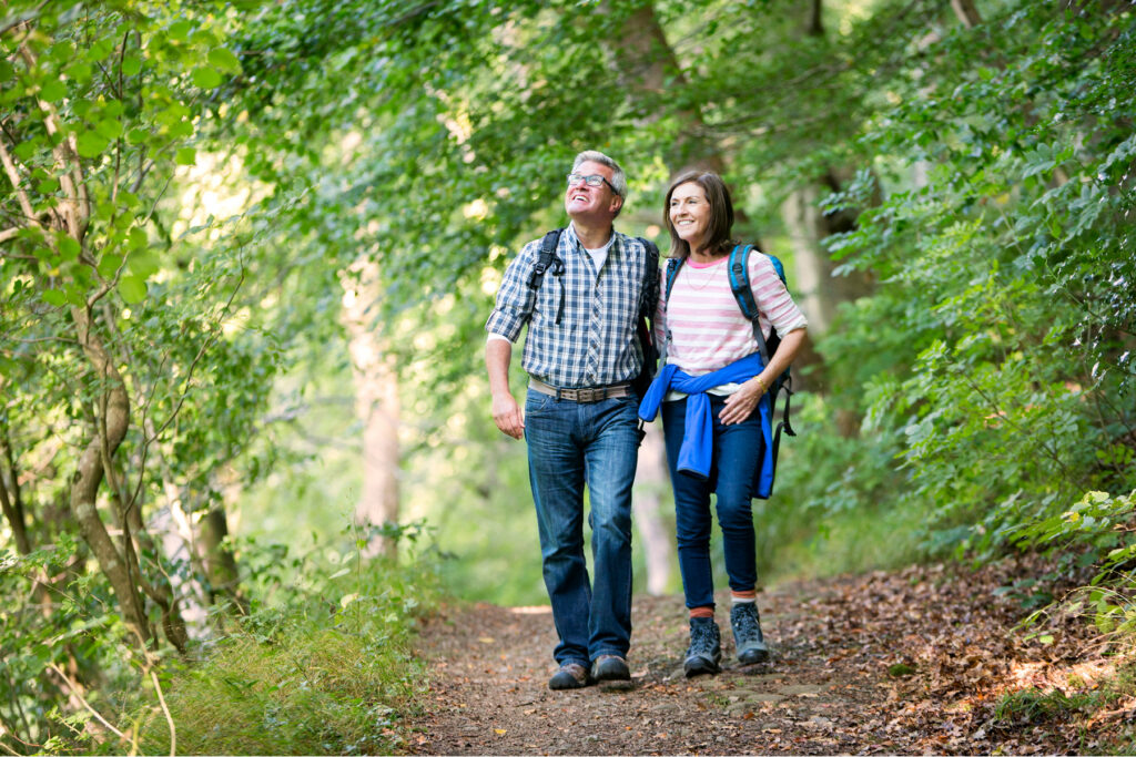 Middle-aged couple smiling and hiking together on a wooded trail in spring